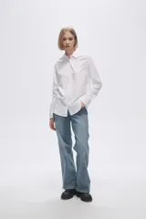 Camisa blanca de manga larga con cuello clásico y cierre frontal con botones. Corte recto y holgado.