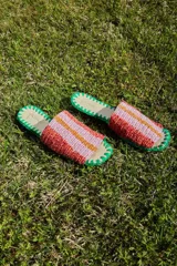 Sandalias bajas con base de cuero y capellada tejida a crochet con rayas horizontales en tonos rosa, naranja y amarillo. La base está ribeteada con hilo de crochet verde.