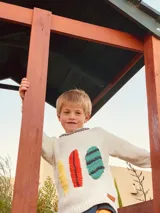 Sweater de lana color crema con cuello redondo y mangas largas. Presenta tres tablas de surf bordadas a mano en amarillo, rojo y turquesa.