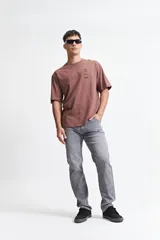 Remera marrón de manga corta con corte oversize y cuello redondo. Estampado en la espalda con diseño abstracto y texto.