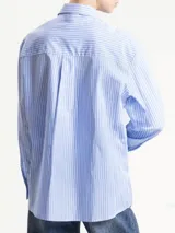Camisa de manga larga con cuello camisero, confeccionada en tela de rayas diplomáticas celestes y blancas. Incluye un corbatín a juego sujeto con un broche tipo camafeo.