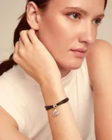 Pulsera Uno de 50 de cuero marrón con tres tiras y dije colgante de corazón plateado con el logo de la marca grabado.