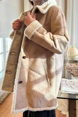 Abrigo gamulán marrón con cuello, solapa, puños y borde frontal de piel sintética blanca. Tiene cierre con botones y bolsillos laterales.