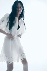 Vestido corto blanco de crepé con secciones de broderie, cuello camisero, botones ocultos, mangas cortas abullonadas, cinturón extraíble y ribete festoneado.