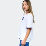 Remera blanca de mujer con cuello y mangas con detalles tricolor (azul, blanco y rojo), logo de Umbro bordado en negro y escudo del Club Nacional de Football estampado.