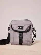 Bandolera gris de nylon con correa negra ajustable y logo Rusty estampado en negro.