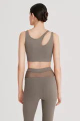 Top deportivo asimétrico color gris topo, realizado en tela doble y cintura elástica para mayor compresión y sujeción.