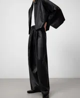 Pantalón negro de piel ovina, tiro alto con cintura cruzada y pinzas delanteras. Presenta volumen en la parte delantera izquierda y pierna ancha con corte horizontal a la altura de la rodilla.