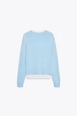 Chaqueta celeste de punto con cuello redondo y manga larga. Tiene cierre frontal con botones y detalle de falsos bolsillos delanteros con ribete blanco.