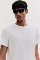 Remera blanca de algodón liviano con cuello redondo ribeteado y bajo recto. Corte ajustado que realza el contorno del cuerpo creando una silueta entallada.