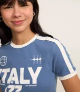 Remera celeste con cuello redondo y mangas cortas con ribete blanco. Estampado frontal con la palabra "Italy" en letras blancas y detalles gráficos.
