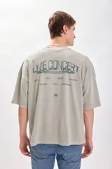 Remera verde de corte amplio y recto, con estampado en el centro de la espalda que incluye el texto "Live Concert" y una lista de géneros musicales.