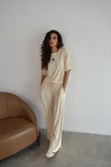 Conjunto de dos piezas color crema, compuesto por una remera de mangas cortas con logo bordado en el pecho y un pantalón palazzo con cintura elastizada y cordón ajustable.