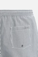 Short de baño con textura seersucker a rayas verticales azul marino y blanco. Tiene cintura elástica ajustable con cordón, bolsillos frontales y traseros, aberturas laterales en el bajo y forro interior.