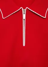 Jersey rojo de punto fino con cuello polo y cierre de cremallera parcial. Tiene manga corta y ribetes blancos en cuello y mangas.