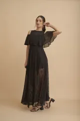 Vestido largo negro con transparencias y encaje. Tiene escote redondo, corte a la cintura y falda larga con paneles de encaje floral. El cuerpo superior es de gasa con hombros descubiertos y volado.