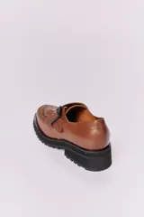 Zapato mocasín color marrón de cuero con hebilla metálica negra y detalle de flecos.