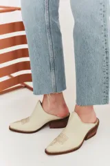 Mules de cuero color crema con punta fina y bordado estilo western en el empeine.