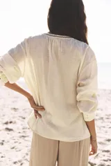 Blusa color crudo de cuello redondo con escote pico y manga larga. Detalle de bordados delanteros y abalorios. Cierre frontal con botones.