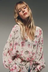 Camisa semitransparente con estampado de flores en tonos rosa y verde, cuello pico y manga larga con puños. Tiene aberturas laterales y cierre frontal con botones.