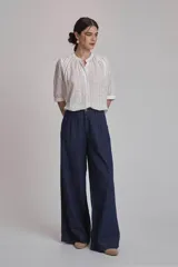 Camisa blanca con estampado de cruces, cuello mao y mangas 3/4 con detalle de pliegues en los hombros. Cierre frontal con botones.