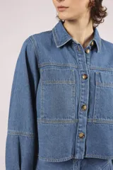 Camisa de denim celeste, de corte cropped, con cuello camisero, mangas 3/4 abullonadas y cierre frontal con botones.