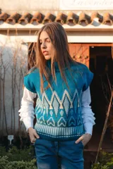 Chaleco tejido con cuello alto, diseño geométrico en tonos celeste y blanco, y corte holgado.