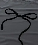 Remera gris de algodón con cuello redondo y manga corta. Presenta un estampado central de un lazo negro.