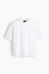 Remera blanca de algodón pesado, corte boxy holgado, cuello redondo ribeteado y hombros caídos.