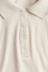 Remera polo color crema de punto acanalado, con cuello clásico, tapeta de botones y mangas cortas. Corte entallado.