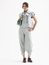 Pantalón de cuero ovino color gris claro, con frunces en el puño de la botamanga que aportan volumen. Tiene cintura doble con pespunte y botones forrados en cuero.