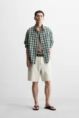 Bermuda color verde militar, de corte relaxed fit, con bolsillos frontales y traseros tipo plaqué, detalle de tira y bolsillo multifunción en la pierna, y bajo irregular.