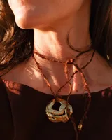 Collar con cordón naranja y dije de flor dorada.