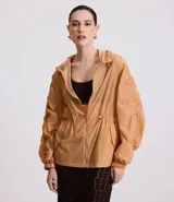 Campera deportiva femenina tipo parka, color ocre, confeccionada en poliamida y poliéster. Tiene cuello con capucha, mangas largas con puños elásticos, cierre frontal con cremallera y cordón ajustable en la cintura.