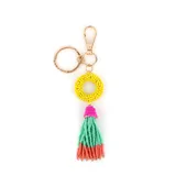 Llavero con aro dorado, cuentas de colores formando un círculo amarillo y borla con cuentas rosas, verdes y naranjas.