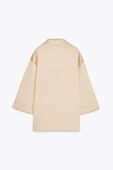 Blazer color beige de cuello solapa y manga tres cuartos. Tejido con efecto arrugado y cierre frontal cruzado con botones negros.