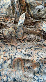 Vestido largo estampado con tirantes finos y escote en V cruzado. Presenta un patrón paisley en tonos tierra, beige y azul, con un lazo ajustable en la cintura y un ruedo con volado.