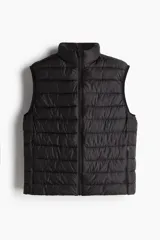 Chaleco negro levemente acolchado en tejido guateado con cuello elevado y cierre con protección para el mentón. Modelo con ribete de cinta elástico en las sisas y bolsillos laterales discretos con cierre. Corte ajustado que realza el contorno del cuerpo creando una silueta entallada.