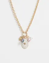 Collar corto dorado con cadena de eslabones gruesos y dijes colgantes: cristal facetado azul, dije dorado con forma de abanico, dije ovalado blanco con corazón dorado y strass, perla rosa y perla blanca.