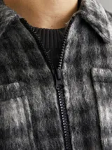 Sobrecamisa corta de manga larga con cuello sport, cierre frontal de cremallera, puños con botones, solapa cortaviento, bolsillos en pecho y delanteros. Diseño a cuadros grises y negros.