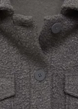 Chaqueta color gris topo de tejido bouclé, con cuello camisero, cierre frontal con botones, dos bolsillos de parche con solapa y botón en el pecho, y mangas largas.