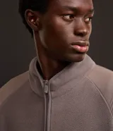 Saco masculino confeccionado en fleece color gris con recortes en marrón y negro, cuello alto, cierre en cremallera, cintura y puños ajustados con elástico. La prenda posee estampa localizada en el pecho con la palabra "LEAGUE".