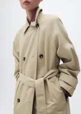 Abrigo largo estilo trench coat color beige, con doble botonadura, cuello de solapa ancha, manga larga con puños abotonados y cinturón desmontable. Presenta un diseño recto y oversize.