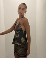 Top halter con escote profundo en V y corte peplum, confeccionado en tejido de malla con estampado tipo tie-dye o desteñido en tonos negro y beige/marrón claro.