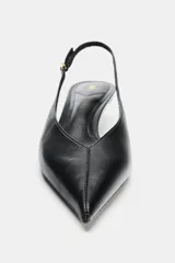 Zapato destalonado negro de punta fina con tacón kitten. Presenta un escote en pico y una tira trasera ajustable con hebilla y elástico.