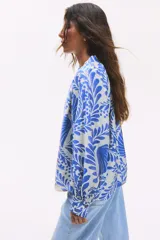 Blusa oversized con cuello elevado fruncido, abertura en V adelante y bajo recto. Mangas globo largas de corte raglán con abertura y botón en los puños. Estampado floral en tonos azules y blancos.