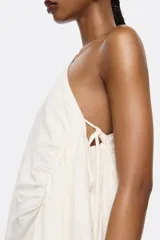 Vestido largo marrón de lino, con corte ajustado y fruncido. Presenta escote de un solo hombro con lazo y maxitira de tejido. Cierre con cremallera invisible lateral y pañuelos laterales.