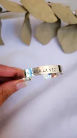 Brazalete rígido de metal plateado con frase grabada.