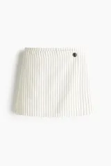 Short pollera mini color blanco con rayas verticales negras, de corte cruzado con botón a la vista y cierre lateral oculto con gancho.