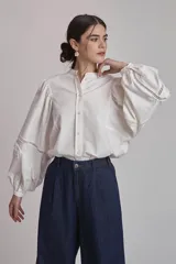 Camisa blanca de mangas largas abullonadas con detalles de calado en los puños, cuello mao y cierre frontal con botones.